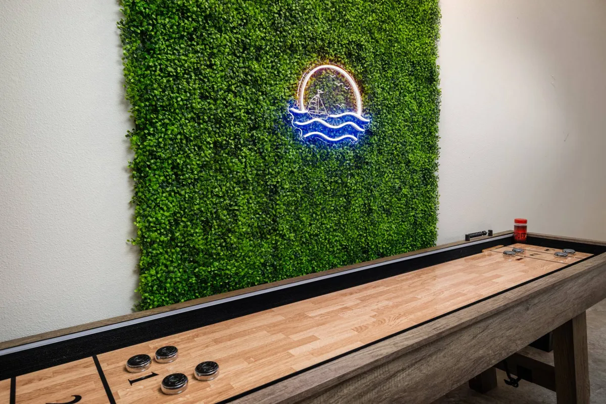 This photo centers on a stylish shuffleboard table, enhanced by neon wall art and lush greenery. The space feels dynamic and modern, designed for socializing, playful competition, and memorable gatherings.