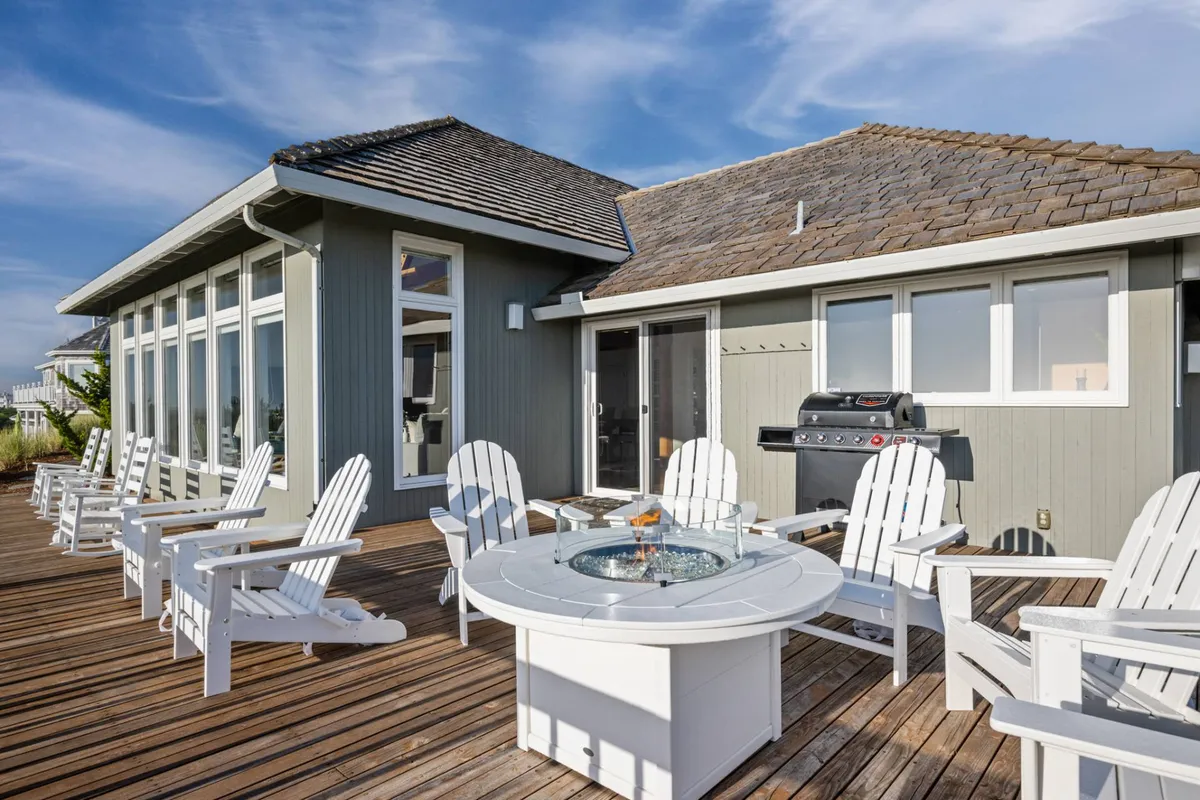 A spacious wooden deck featuring a fire pit, Adirondack chairs, and a grill. The deck overlooks scenic surroundings, offering a comfortable space for outdoor dining, barbecues, and socializing as a group.