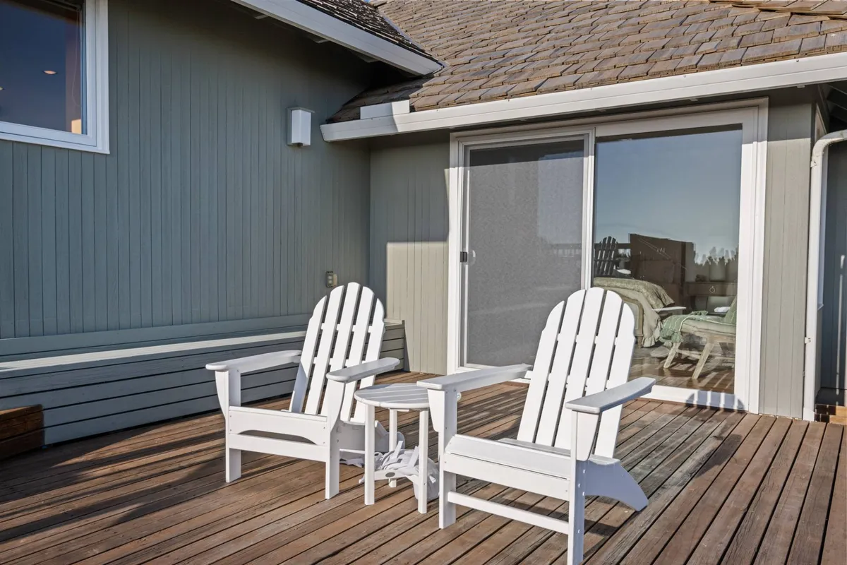 A tranquil outdoor seating area features white Adirondack chairs and a small side table, set against the backdrop of sliding glass doors. The space invites guests to relax, unwind, and take in the surrounding natural beauty—ideal for planning excursions or reflecting on a day spent exploring local attractions.