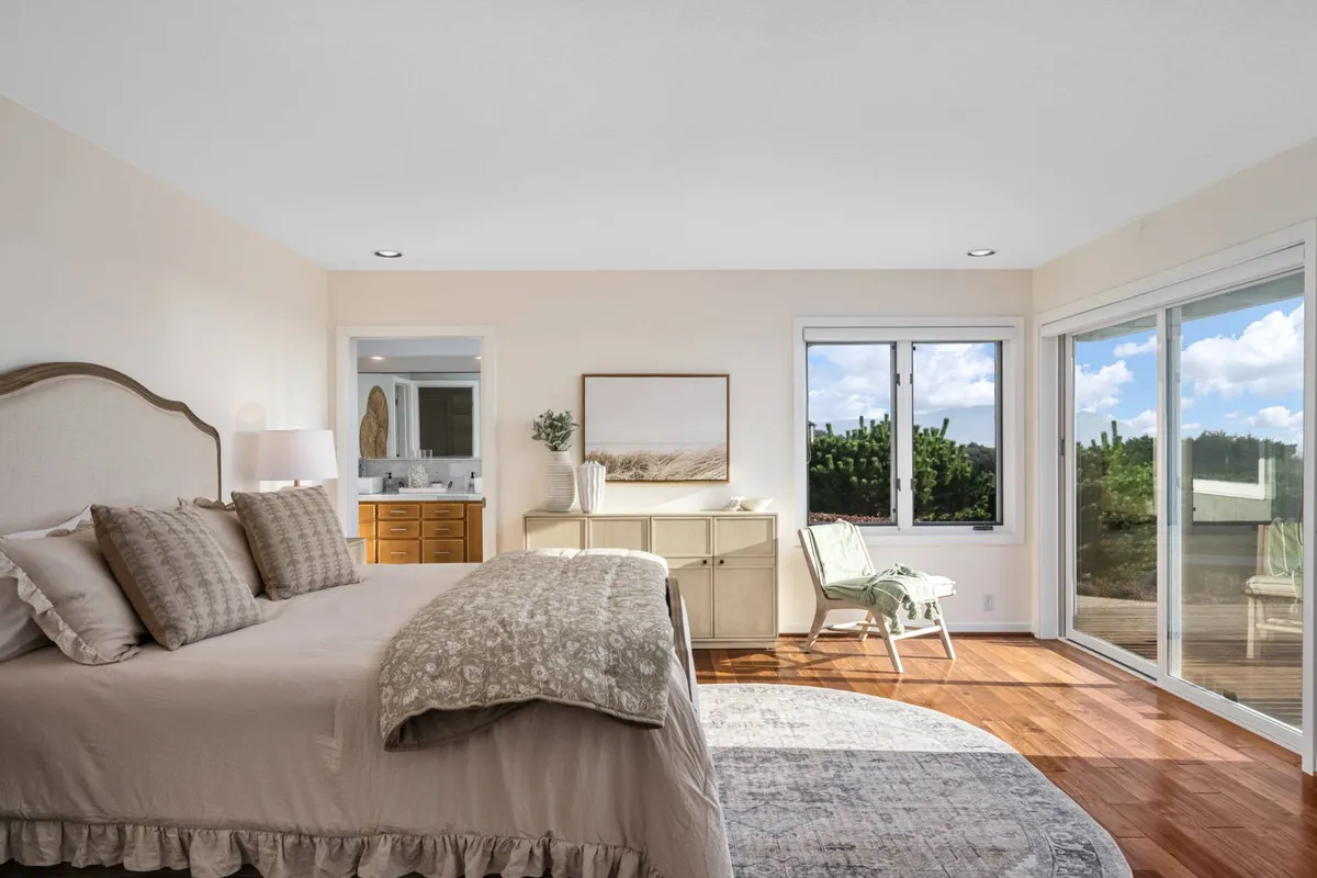 A beautifully styled bedroom featuring a plush bed with decorative pillows, large windows that invite natural light, wooden flooring, and tasteful wall art. The tranquil ambiance is perfect for relaxation and privacy.
