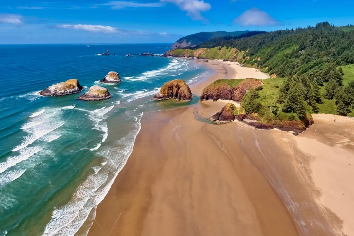 A breathtaking Oregon coastal landscape with dramatic rock formations, gentle waves, sandy beach, and bordering forest. The natural scenery embodies the wild beauty of the Pacific, just a short walk away from the home.