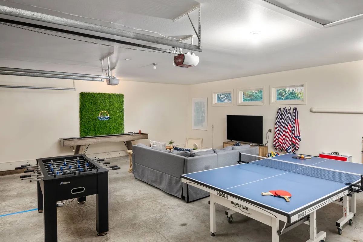 This image showcases a vibrant game room featuring a ping pong table and foosball table, with a comfortable sofa and green wall art. The space exudes a fun and relaxed vibe, inviting people to engage in games, relax, or watch TV.