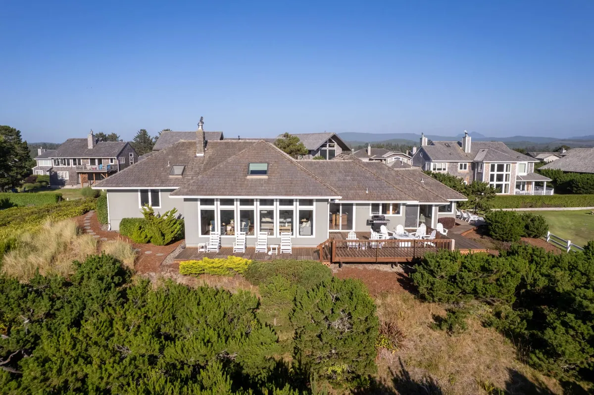 A wide view of the property's spacious deck, large windows, and meticulously landscaped garden. The deck invites groups to gather, relax, and enjoy seamless indoor-outdoor living, further supporting the concept of shared vacation experiences.