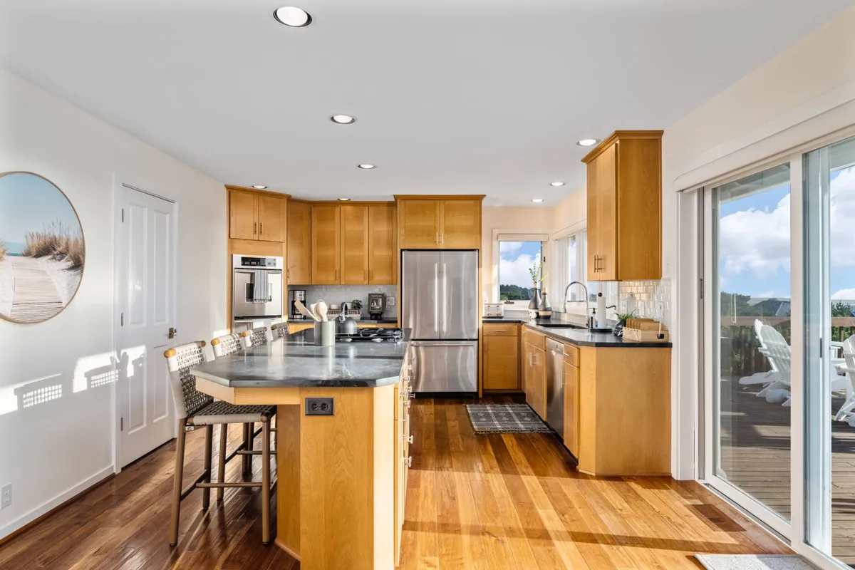 A bright, welcoming kitchen centered around a spacious island with seating, featuring stainless steel appliances and large windows flooding the space with natural light.