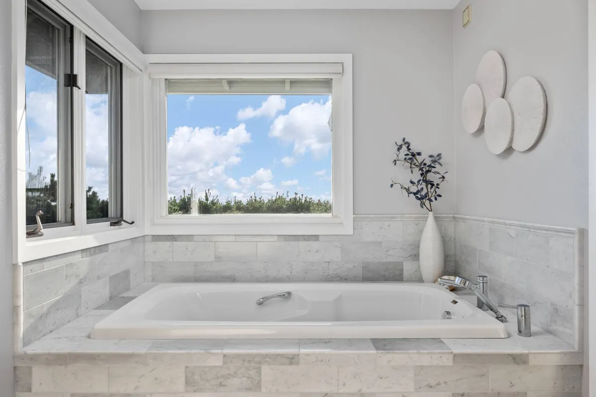 A freestanding bathtub positioned by a window providing scenic views, complemented by a decorative vase. The setting exudes tranquility and invites meditative moments of self-care.
