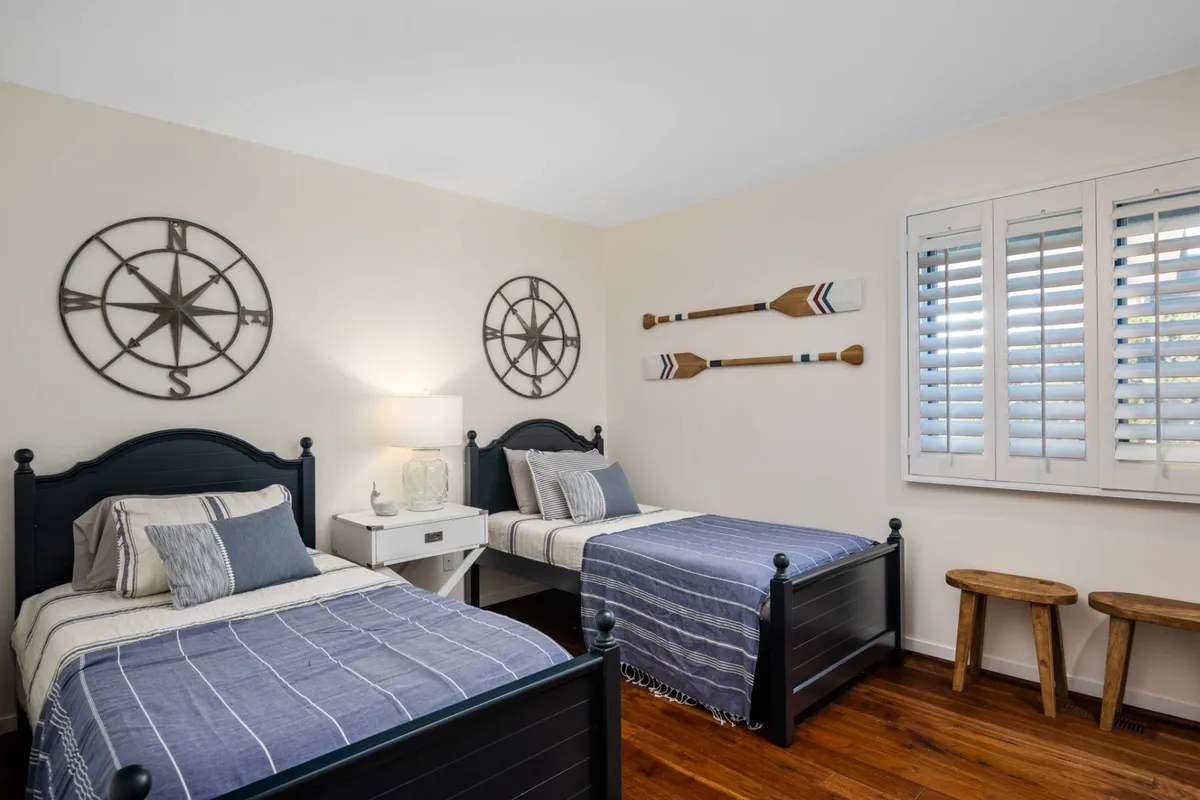 A cozy twin bedroom with two matching beds in dark blue frames, nautical-themed decor, and decorative paddles on the wall. The space feels inviting and family-friendly, ideal for children or friends.