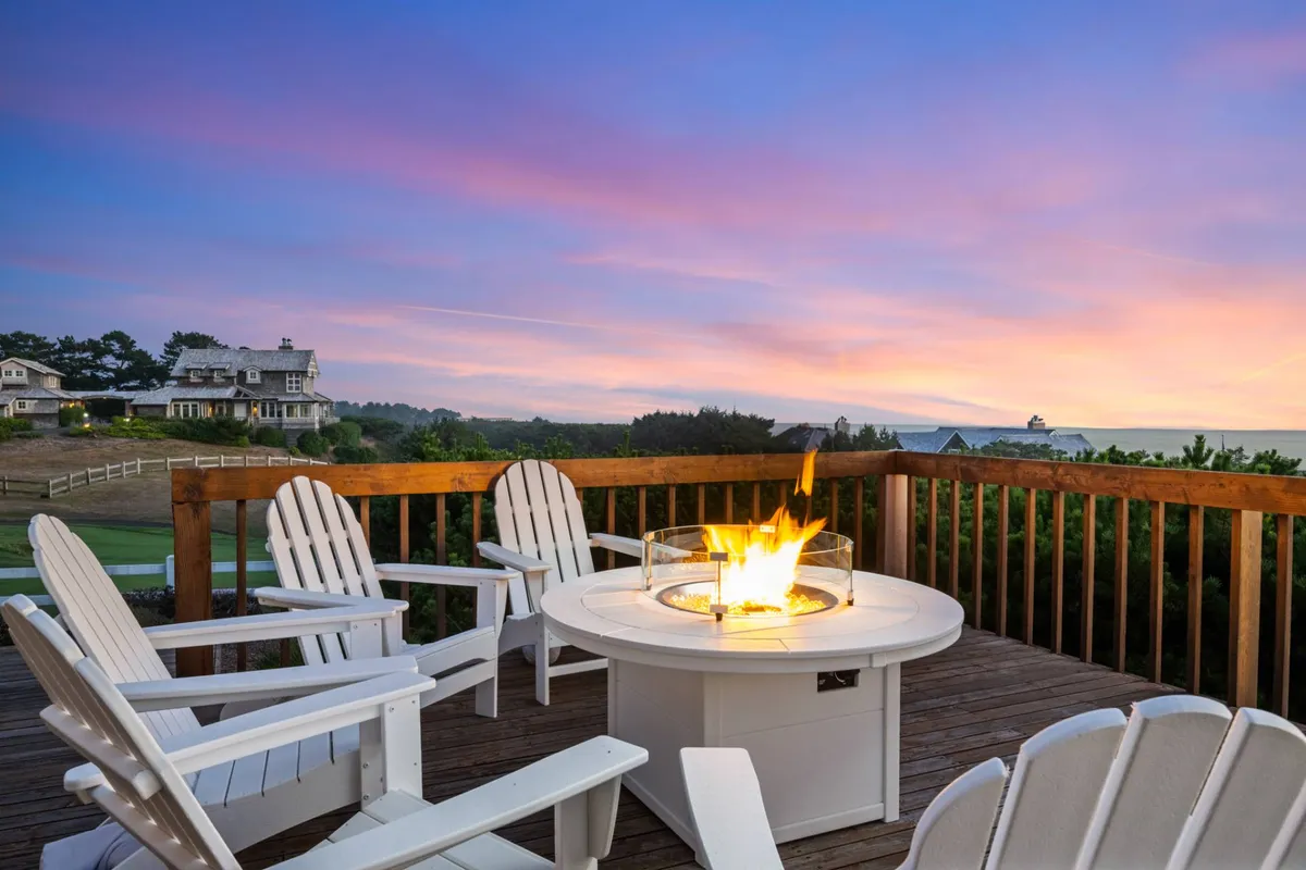 An inviting exterior scene with a fire pit surrounded by Adirondack chairs, set against a vibrant sunset sky. The setup encourages group gatherings, conversation, and shared experiences in the outdoors, highlighting the social and communal aspects of the property.