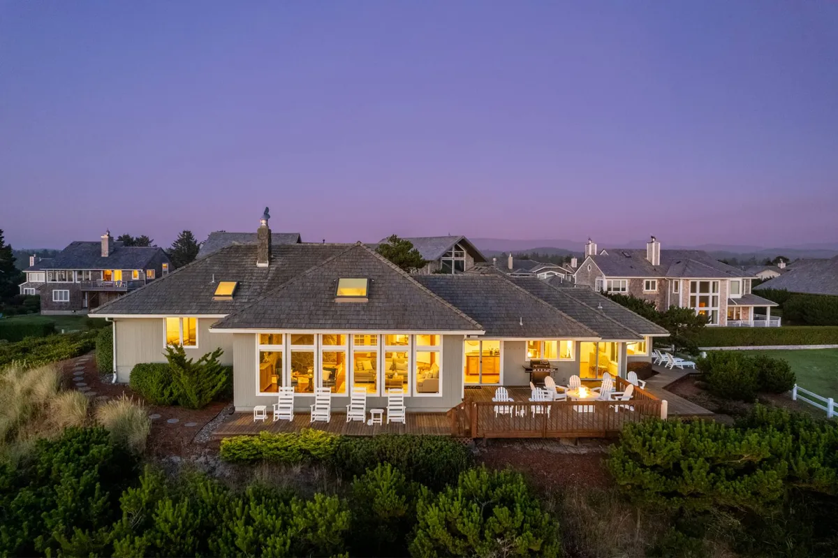 An exterior shot of the home’s deck area with comfortable seating, surrounded by greenery, and featuring expansive windows. The setup is ideal for enjoying the sunset, outdoor dining, and relaxing with friends or family while taking in the view.